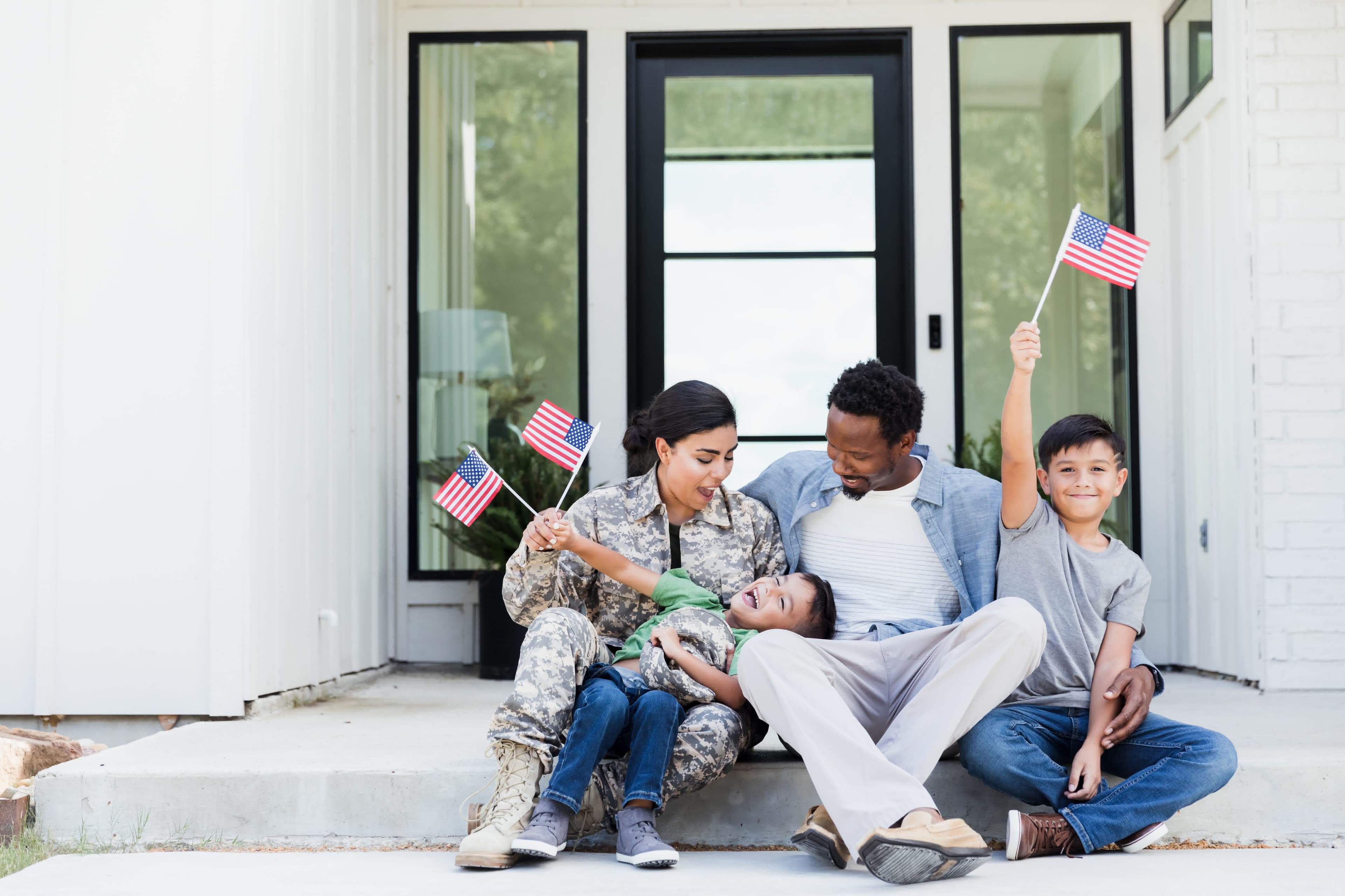 A military family waving American flags on the front steps of their VA-financed home