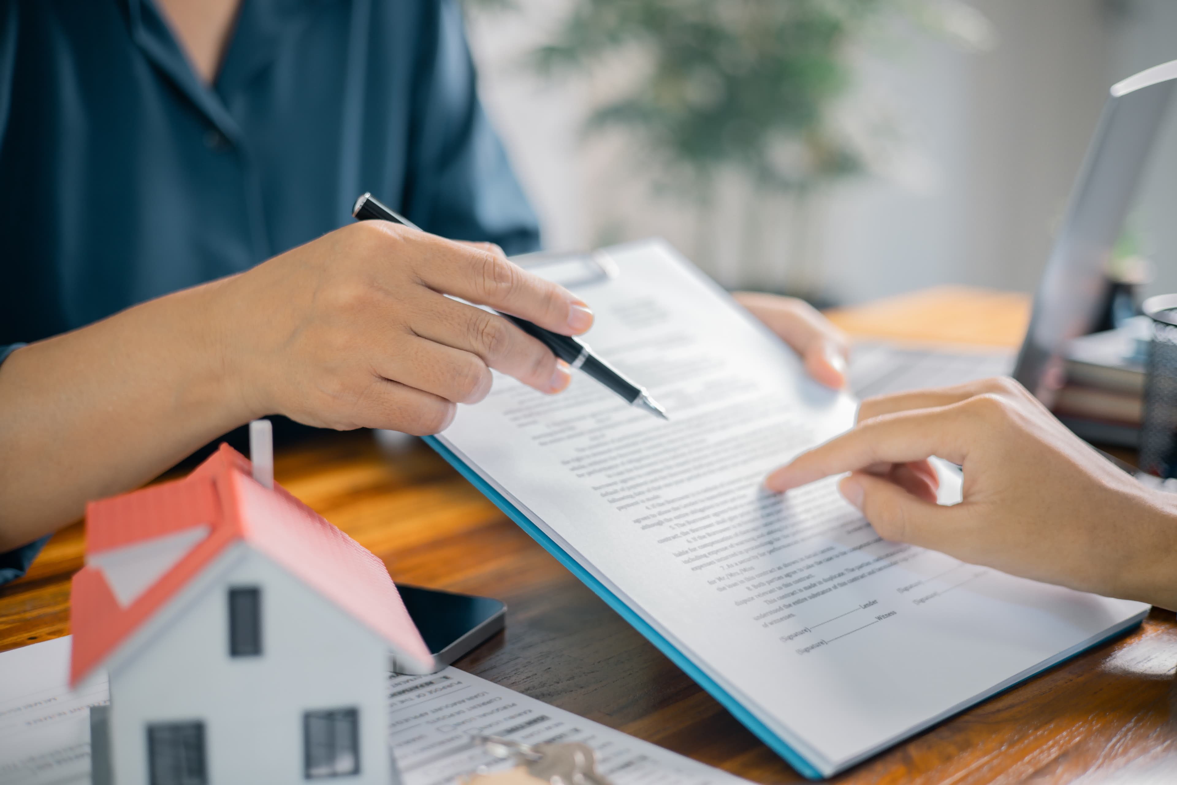 Hands organizing the documents and a model house needed for a California mortgage