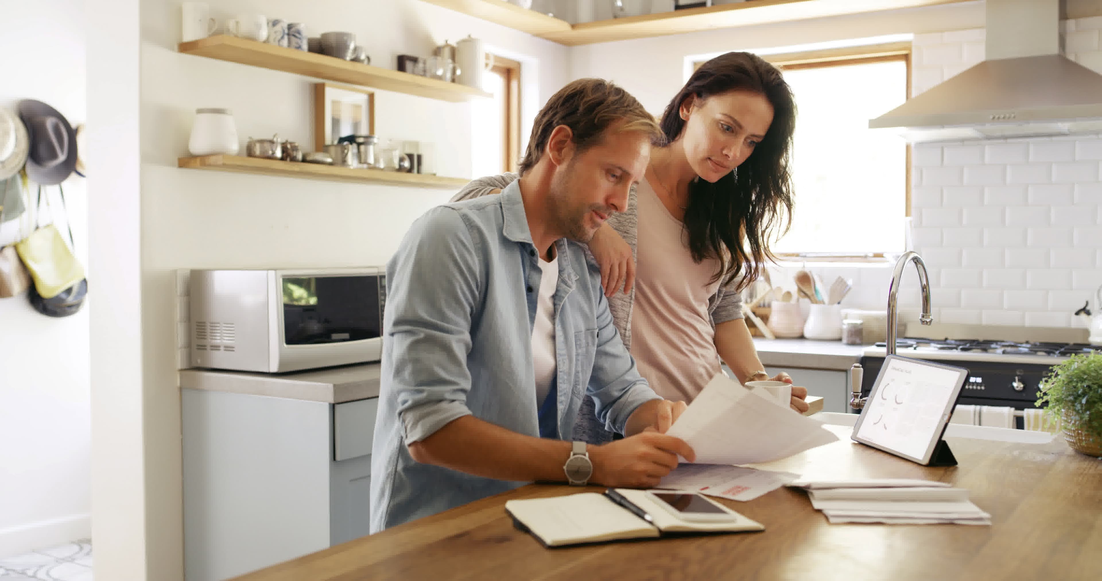 California homeowners comparing bills and charts on a tablet to decide if refinancing is worth it