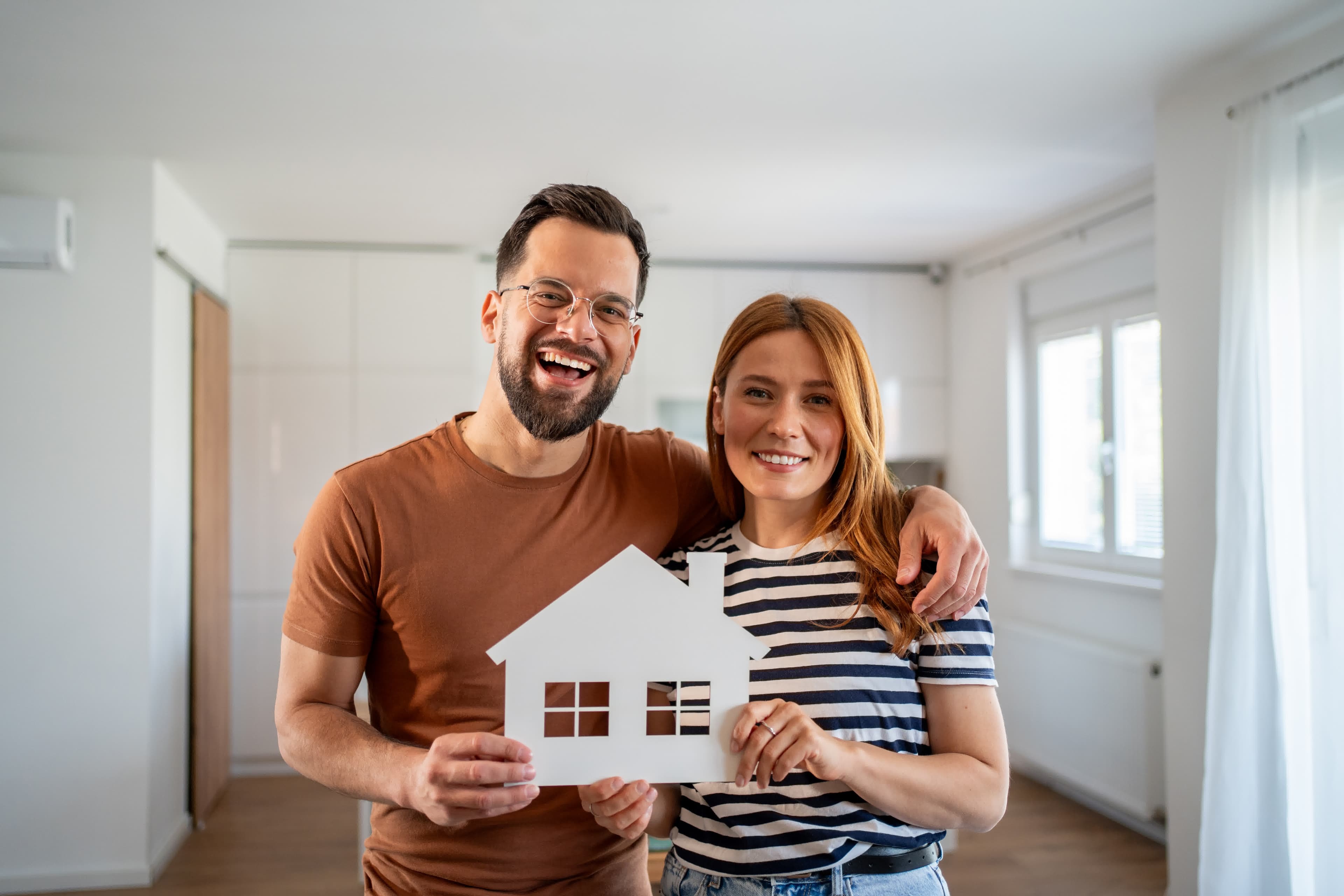 A happy couple holding a paper house cutout after getting a conventional loan